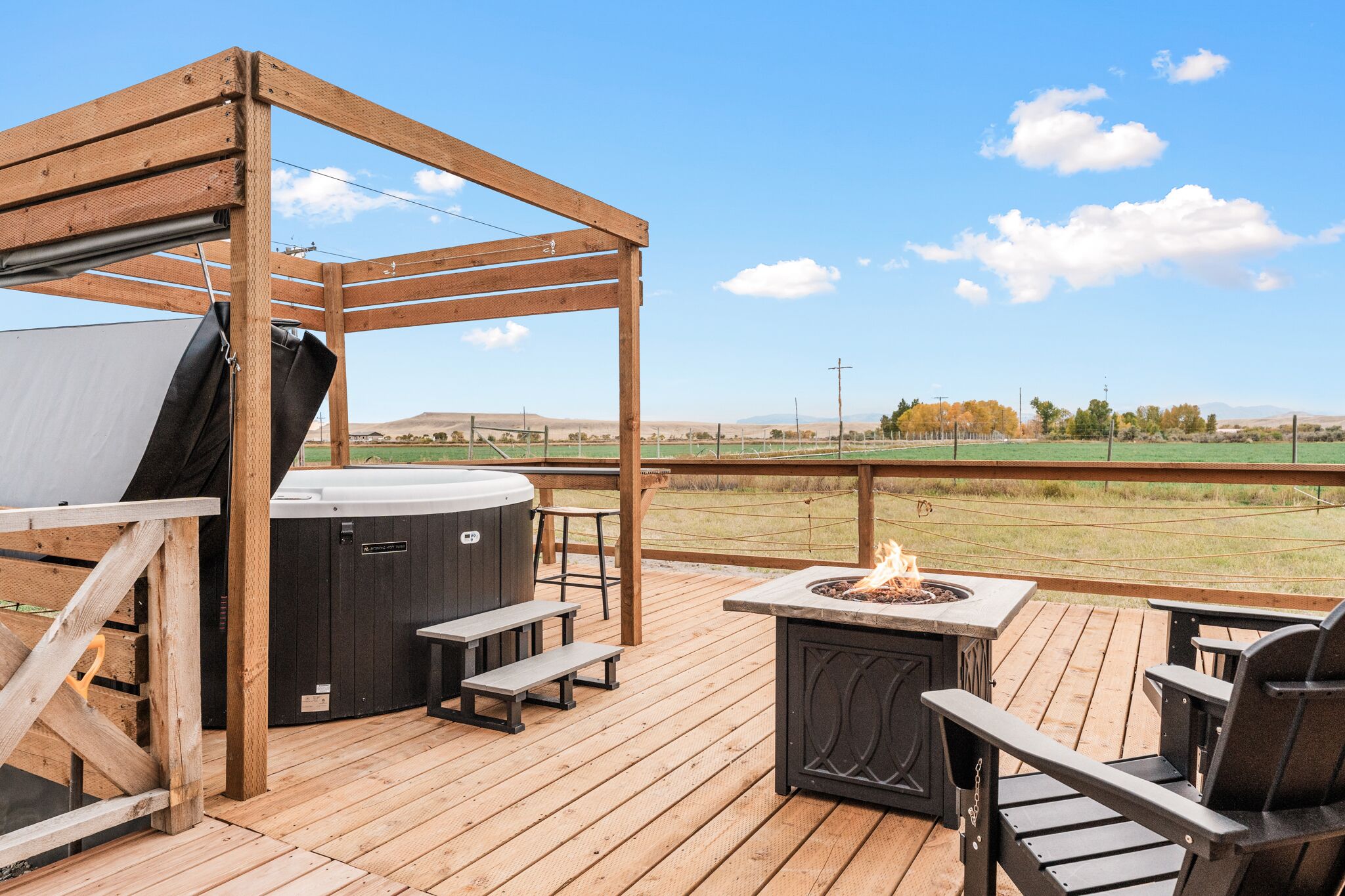Una terraza de madera con hidromasaje, asientos exteriores y una chimenea.