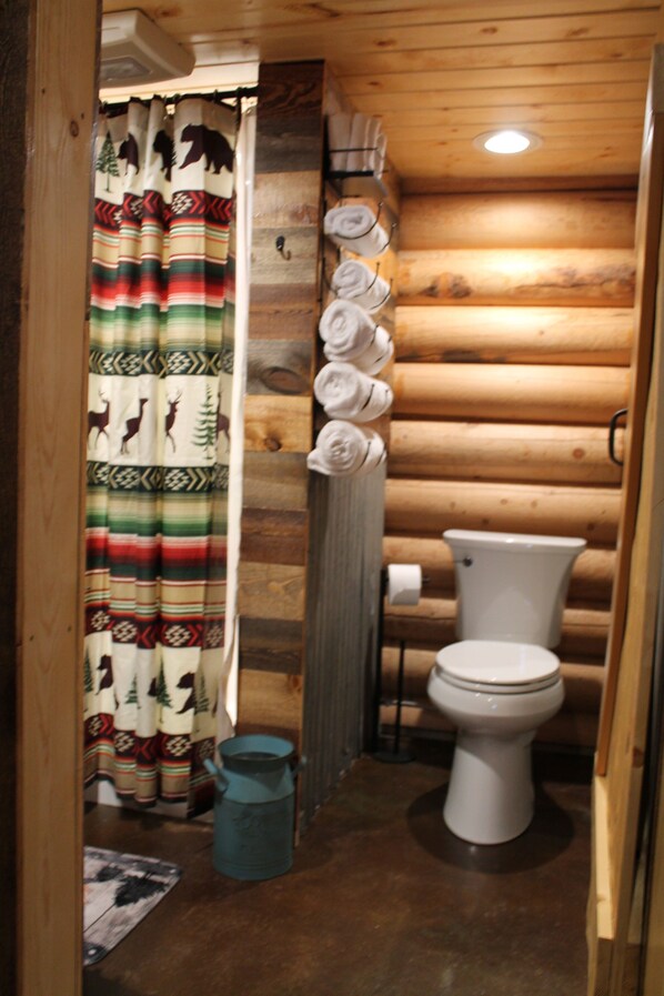 A wooden cabin bathroom with a toilet, a shower curtain with animal prints, and towels hanging on a rack. - LITTLE LOG CABIN IN THE RUBY (Sheridan)