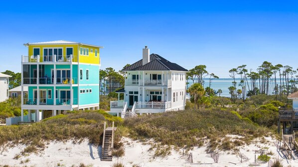 A multi-story beachfront property with balconies, a staircase, and a view of the ocean.