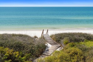 A wooden boardwalk leading to a beach with clear water and a distant island.