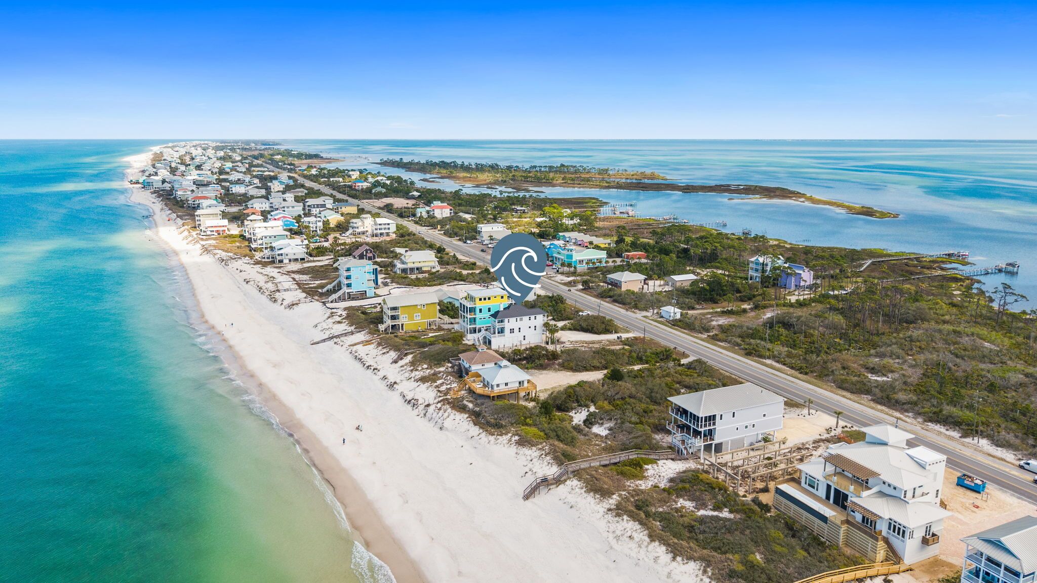 An aerial view of a coastal area with a beach, houses, and a road.