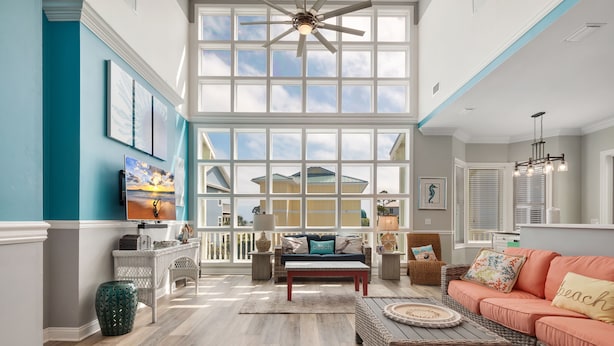 A spacious living room with a large bay window, a ceiling fan, and a view of a house.