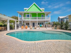 Une maison à deux étages, avec une façade verte et une piscine à l’avant.