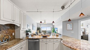 A kitchen with granite countertops, white cabinets, and a dishwasher. There is a ceiling fan and pendant lighting. - Gulfisde Escape: Beachfront Condo in Indian Pass, Community Pool, Pet Friendly (Cape San Blas)