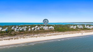 An aerial view of a coastal area with a beach, ocean, and a cluster of white buildings surrounded by greenery. - Gulfisde Escape: Beachfront Condo in Indian Pass, Community Pool, Pet Friendly (Cape San Blas)