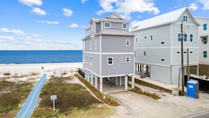 A beachfront property with a two-story building, a covered deck, and a blue pathway leading to the beach.