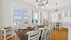 A dining area with a wooden table set for six, white chairs, and a chandelier.