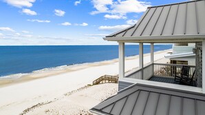 A beachfront property with a covered porch, a wooden staircase leading to the beach, and a view of the ocean.