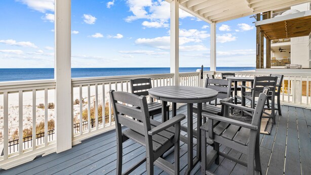 A covered outdoor deck with wooden furniture and a view of the beach and ocean.
