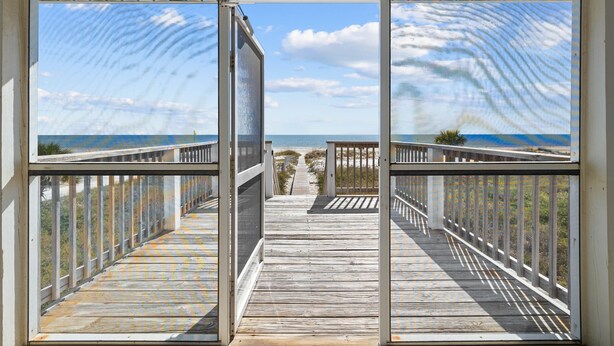 A wooden boardwalk leading to a beach with a clear sky and ocean view.