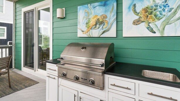 Une cuisine équipée d’un barbecue en acier inoxydable, de meubles blancs et ornée de deux tableaux représentant des tortues de mer.