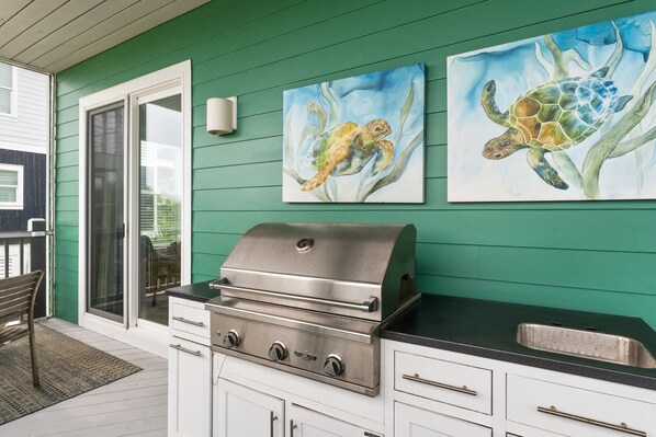 Een keuken met een roestvrijstalen grill, witte kasten en twee schilderijen van zeeschildpadden.