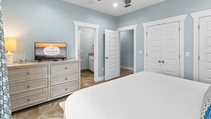 Une chambre à coucher comprenant un lit, une commode, un téléviseur et un ventilateur de plafond.