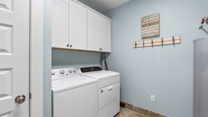 Une buanderie avec un lave-linge et un sèche-linge blancs, un mur bleu et une décoration en forme de nuage de mots.