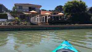 Un kayak sur une étendue d’eau calme, avec une maison et des parasols en arrière-plan.