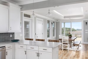 Une cuisine moderne avec des meubles blancs, un plan de travail en marbre et un coin repas comprenant une table et des chaises en bois.