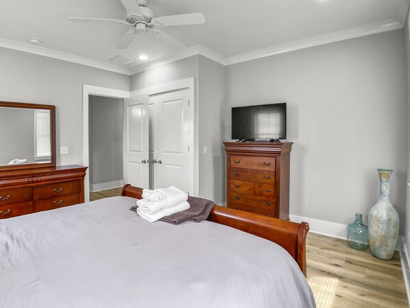 Une chambre à coucher comprenant un lit, une commode, un téléviseur et un ventilateur de plafond.