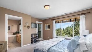 Un dormitorio con una cama grande, una ventana con vistas a árboles, un escritorio pequeño y una puerta que da a un baño.