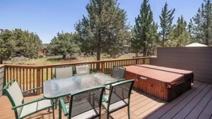 Una terraza con mesa y sillas de vidrio, un jacuzzi y vista a árboles.
