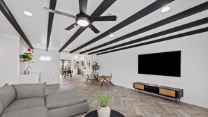 A modern living room with a sectional sofa, a black coffee table with a plant, a ceiling fan, and a flat-screen TV mounted on the wall. - This Must Be The Place ! (Phoenix)