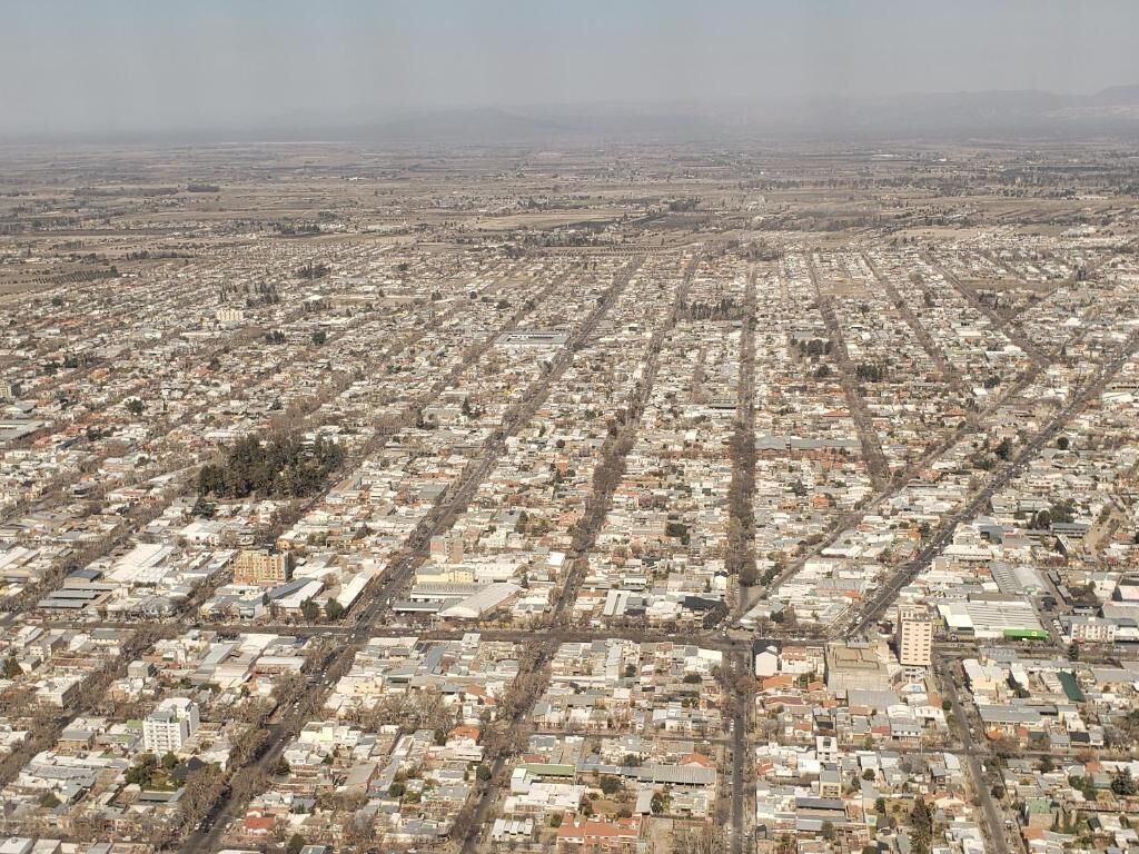 Vista aèria d'una ciutat amb un traçat de carrers en forma de graella, nombrosos edificis i una cadena de muntanyes a la llunània.