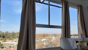 A room with a large window, curtains, a table, and a chair. - NEVADO PENHOUSE BY BOOKHAP (San Rafael)