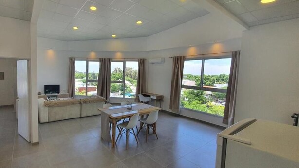 A spacious living area with a sofa, dining table, and chairs, large windows with curtains, and a TV. - NEVADO PENHOUSE BY BOOKHAP (San Rafael)