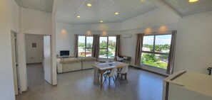 Àmplia zona d'estar amb sofà, taula de dinar i cadires, grans finestres amb cortines i televisió.