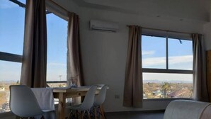 A room with a dining table and chairs, a sofa, and large windows offering a view of the landscape. - NEVADO PENHOUSE BY BOOKHAP (San Rafael)