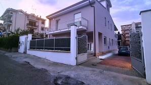 Un edificio residenziale con cancello, un balcone e un'auto parcheggiata nel vialetto.