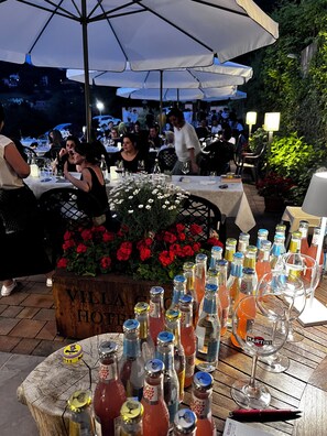 An outdoor dining area with tables, umbrellas, and a variety of bottles and glasses. - Villa Clorè Hotel & Spa (Lama Mocogno)