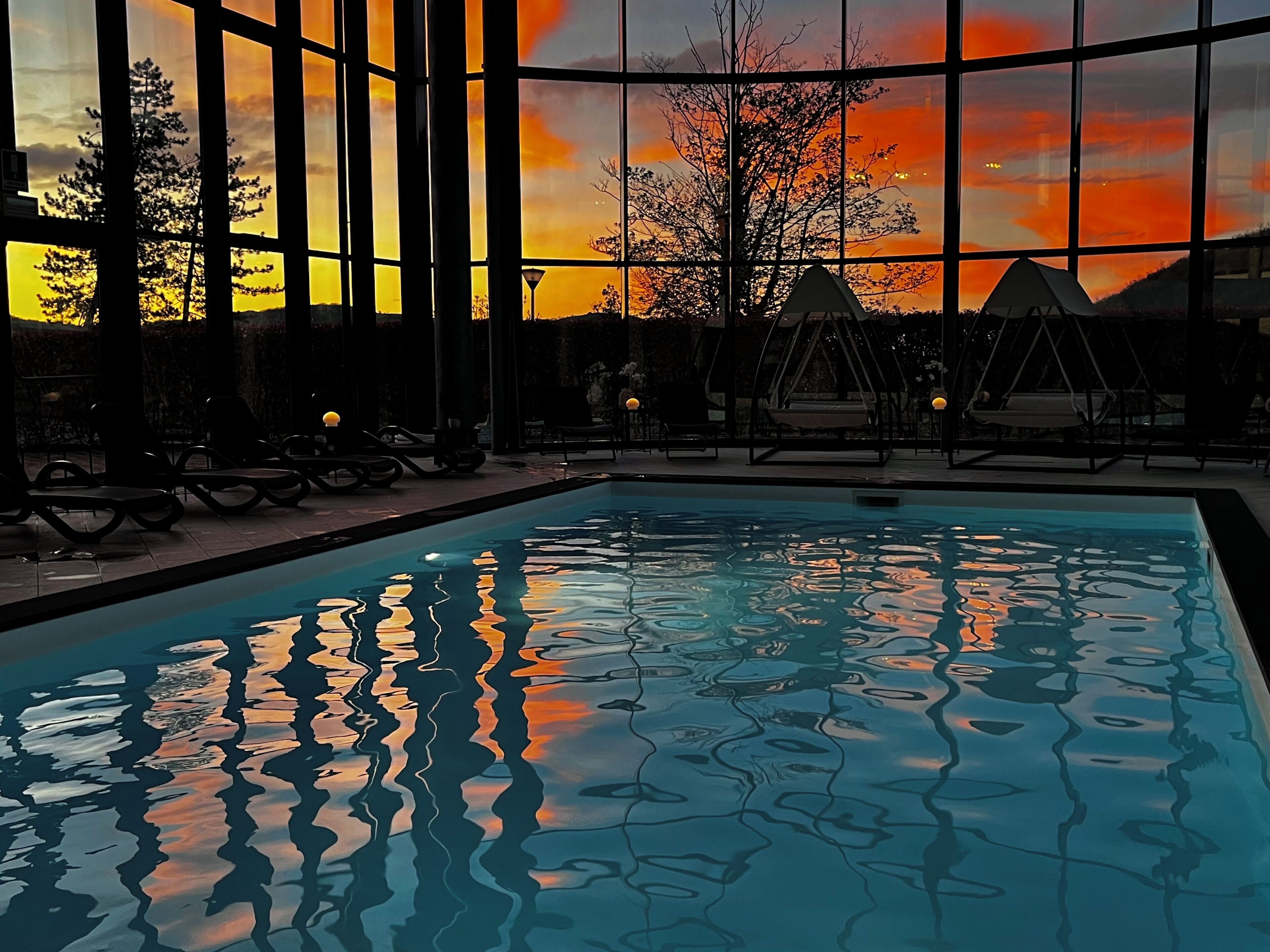 A swimming pool with a sunset view through large windows, lounge chairs, and a swing area.
