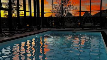 A swimming pool with a sunset view through large windows, lounge chairs, and a swing area.