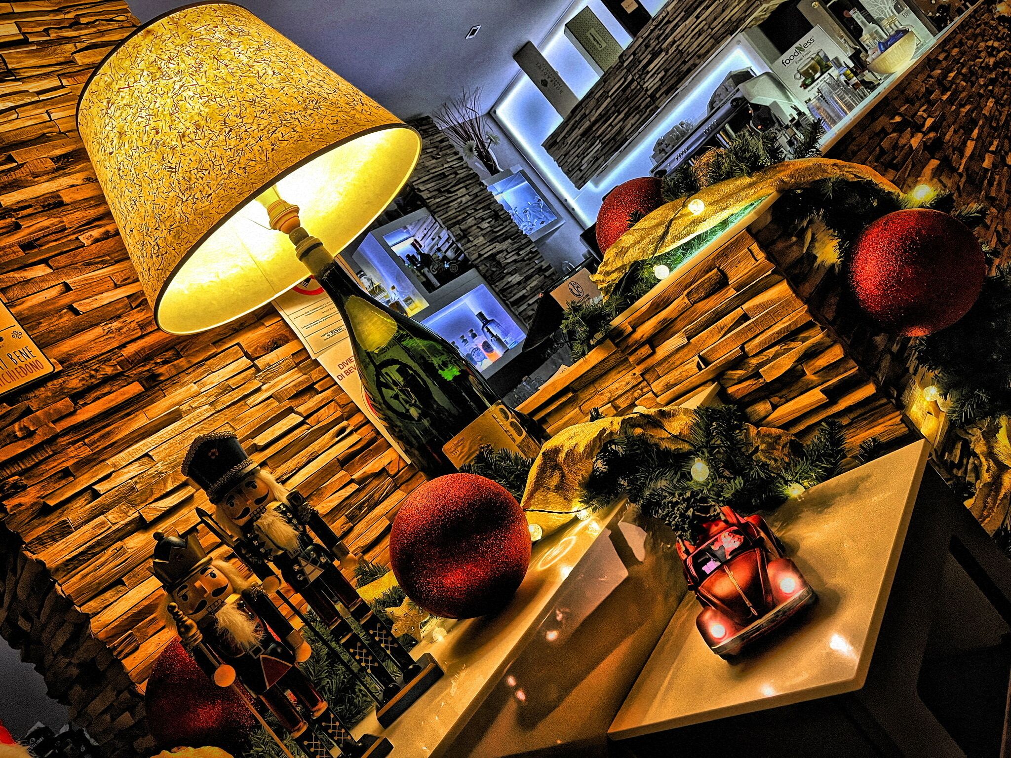 A warmly lit room with a large decorative lamp, wooden wall panels, and festive decorations including red ornaments and a small Christmas tree.
