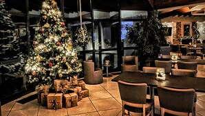 A cozy restaurant with a large Christmas tree and presents, wooden beams, and a stone fireplace. - Villa Clorè Hotel & Spa (Lama Mocogno)