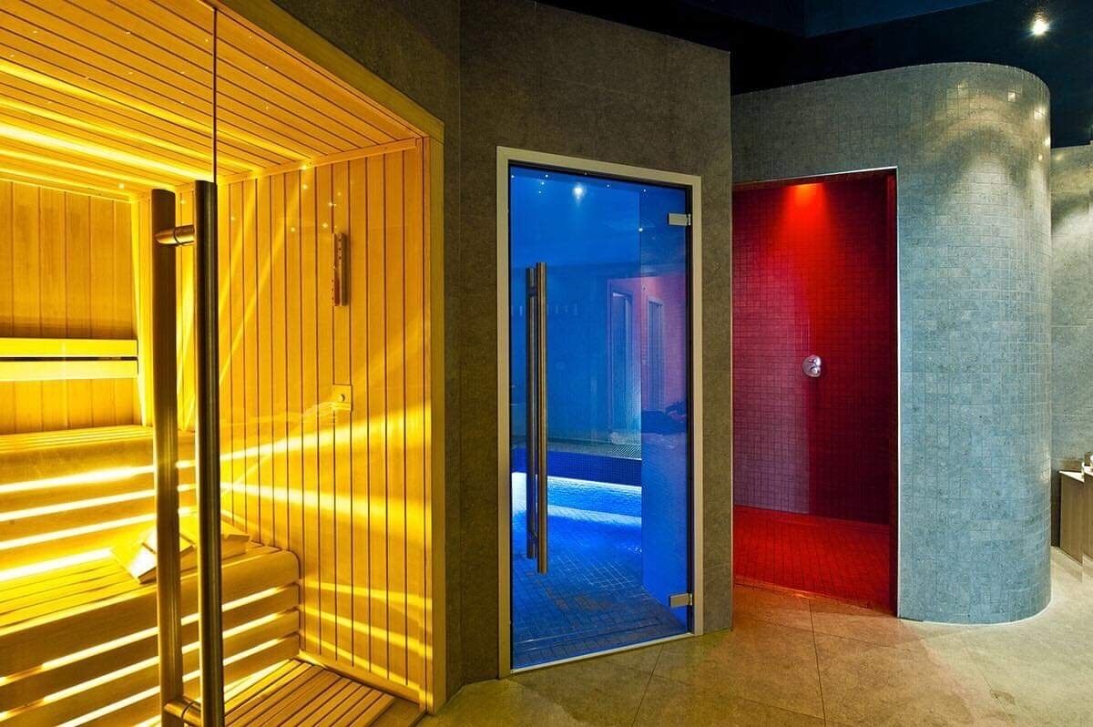 Un espace sauna avec des panneaux en bois et une porte en verre donnant sur un espace piscine.