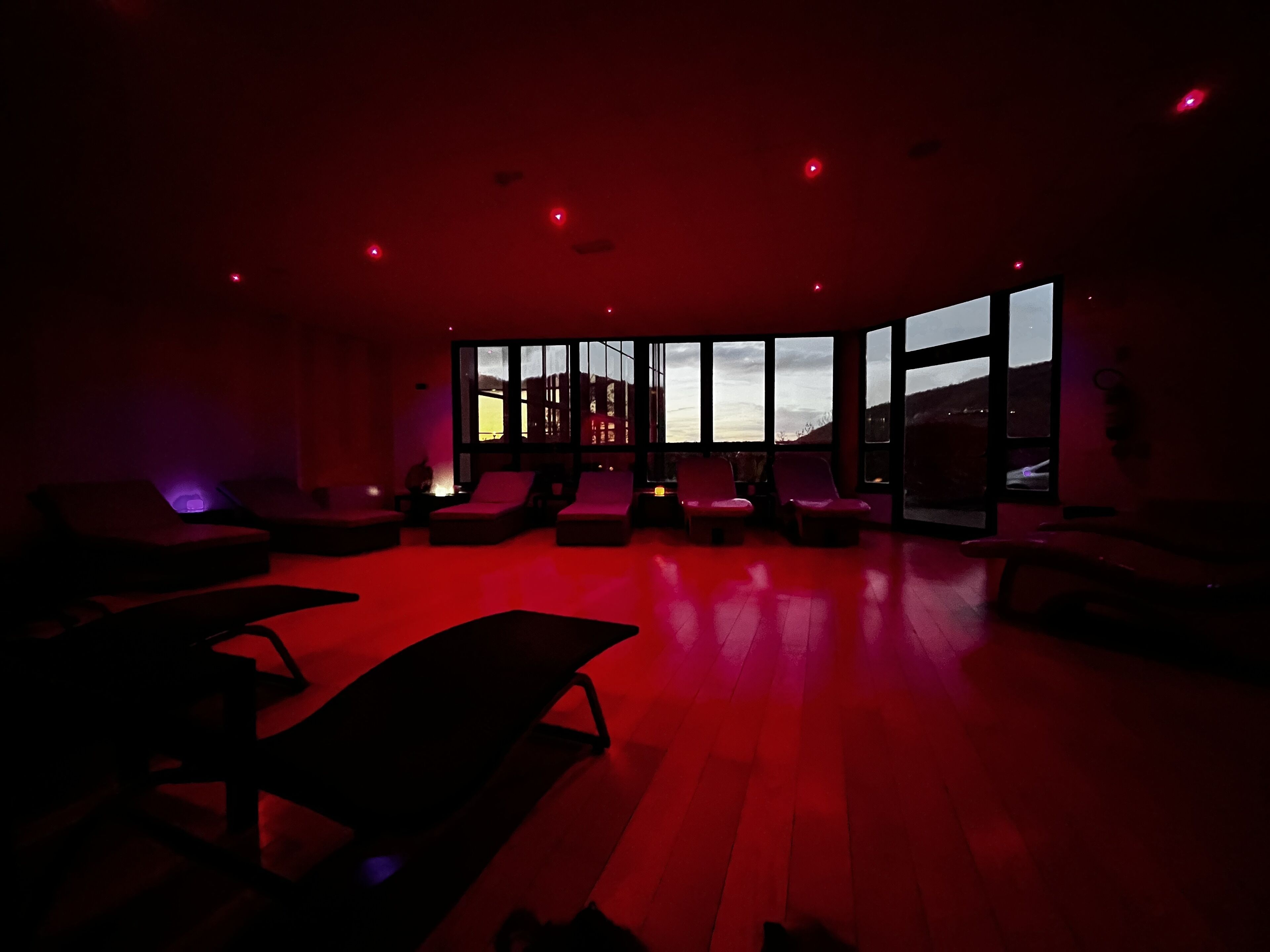 A modern room with large windows, a red-lit floor, and multiple seating areas.