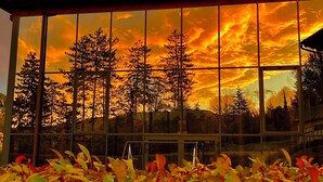 A building with large windows reflecting a sunset and trees. - Villa Clorè Hotel & Spa (Lama Mocogno)