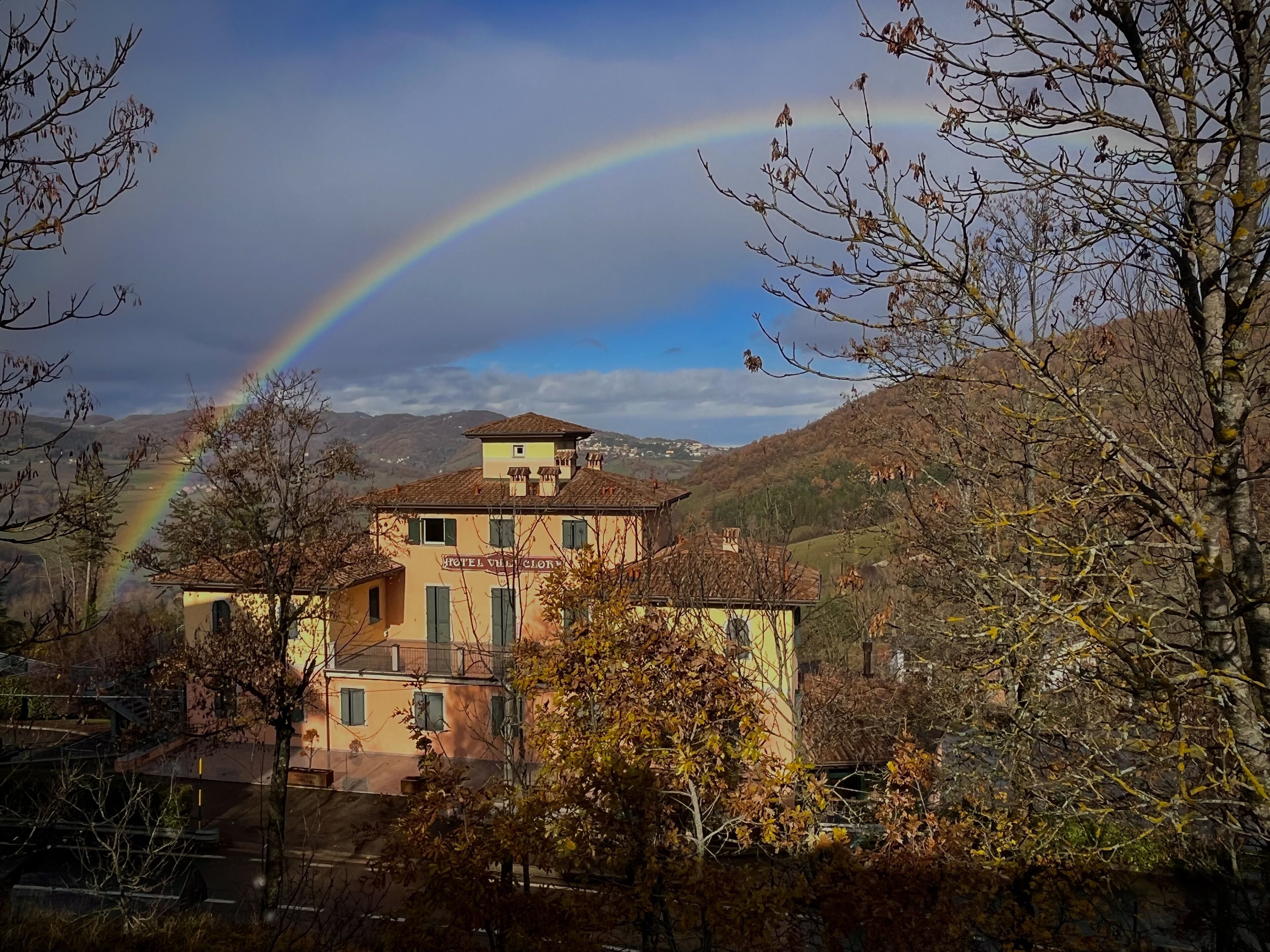 Ein Hotel mit sichtbarem Namen, umgeben von Bäumen und Hügeln, mit einem Regenbogen im Hintergrund.
