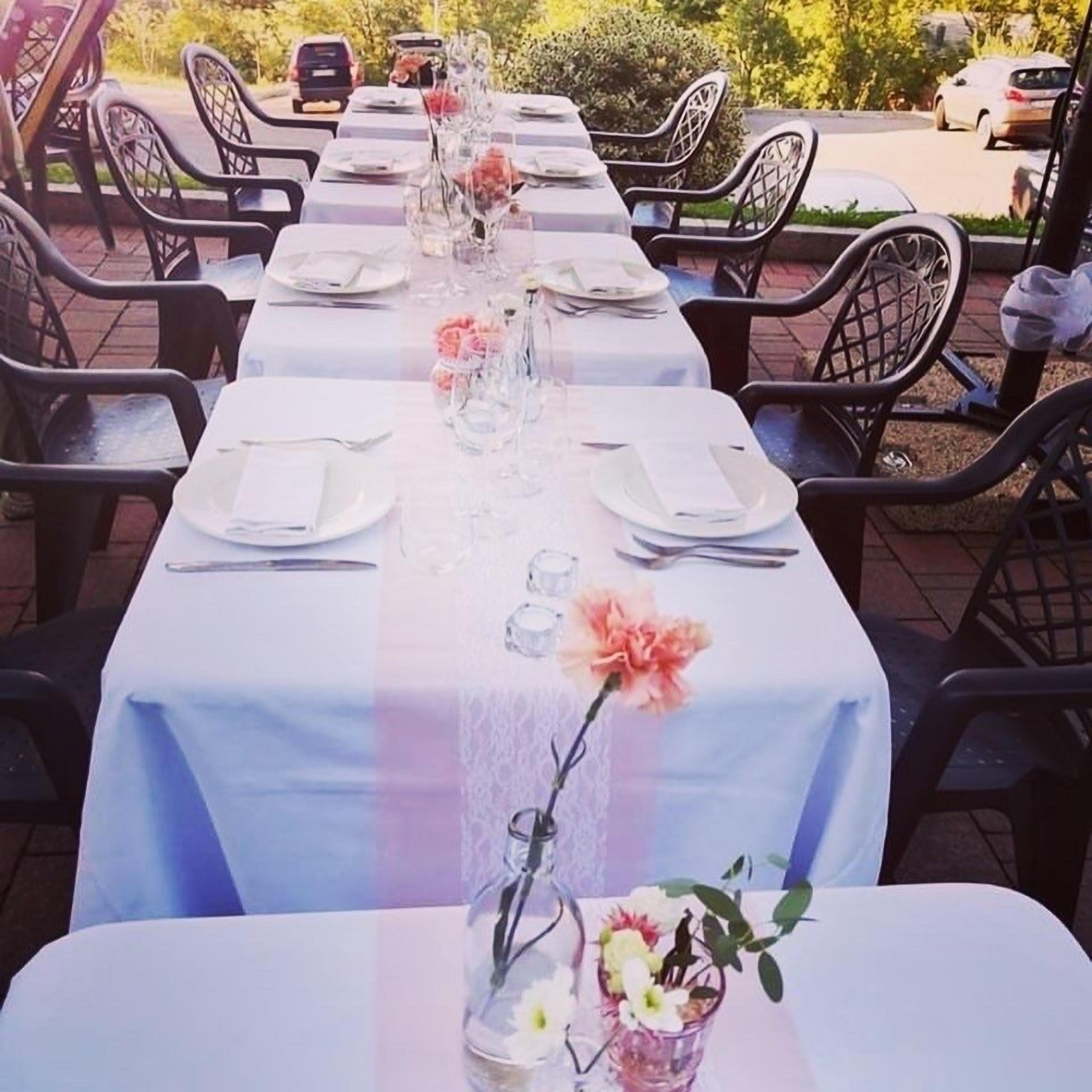 Una larga mesa para comer al aire libre con sillas, mantel blanco y centros de mesa florales.