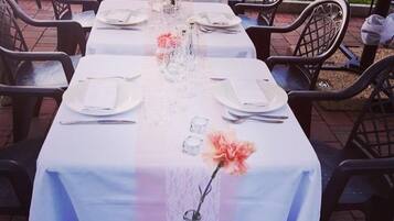 Una larga mesa para comer al aire libre con sillas, mantel blanco y centros de mesa florales.