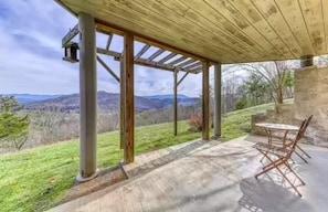 A covered outdoor patio with a table and chairs, overlooking a hilly landscape.