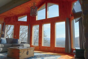 A spacious room with large windows, a wooden ceiling, and a cozy seating area with a sofa and a chest of drawers.