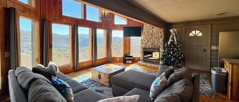 A cozy living room with a fireplace, a Christmas tree, and large windows offering a mountain view.