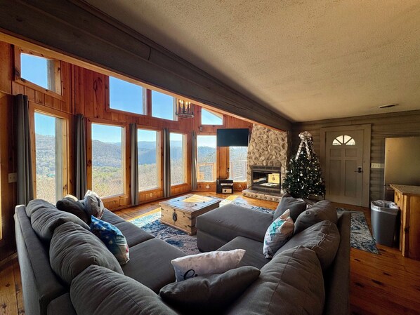 A cozy living room with a fireplace, a Christmas tree, and large windows offering a mountain view.