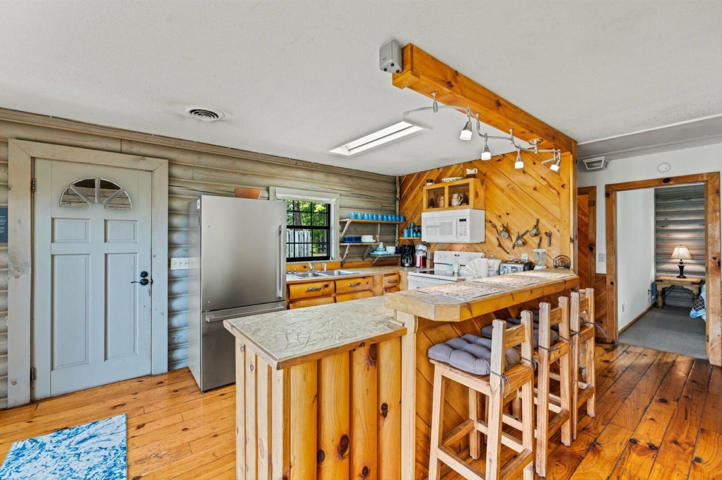 Una cocina con detalles de madera, un refrigerador, un microondas y una zona de bar con taburetes.