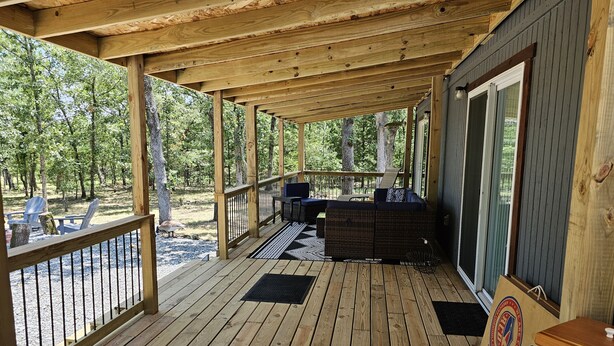 Una terraza de madera con mobiliario exterior, una parrilla y vistas del bosque circundante.