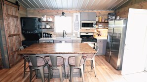 Una cocina rústica con una mesa y sillas de madera, estufa, microondas y refrigerador.
