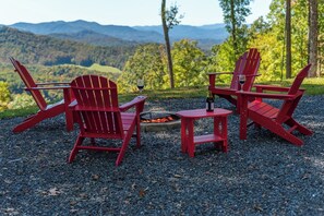A red Adirondack chair set on a gravel surface with a fire pit and a bottle of wine. - Stunning Mtn Views, Hot Tub+Fire Pit, WiFi, Grill! (Bakersville)