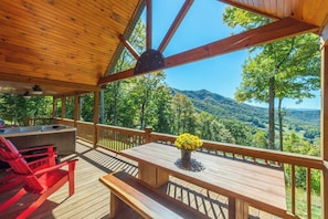 A wooden deck with a hot tub, red chairs, and a table with yellow flowers. - Stunning Mtn Views, Hot Tub+Fire Pit, WiFi, Grill! (Bakersville)